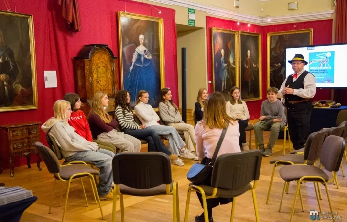 Michał Umłąwski opowiada o muzyce dudziarskiej młodzieży siedzącej w kręgu